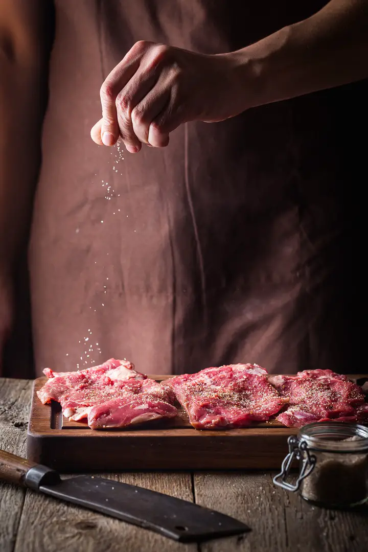 Man Sprinkling Salt On Meat Stakes